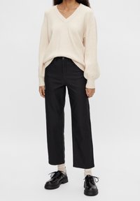 Beige geribbelde gebreide v-hals trui met lange mouwen, gecombineerd met hoge zwarte tapse broek en zwarte veterschoenen.