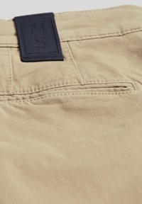 Beige katoenen stof met een achterzak met zichtbare stiksels en een marineblauwe leren label met de aanduiding "M5" op de tailleband.