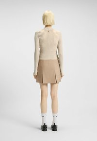 Beige gestreepte geribbelde blouse met lange mouwen, gecombineerd met een tan kleurige geplooide minirok. Zwarte schoenen met textuuraccenten en witte sokken met logo.