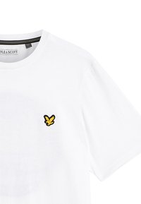 Hvid kortærmet T-shirt med lille gult fuglelogo på venstre bryst og sort-gul stribet inderside af kraven.