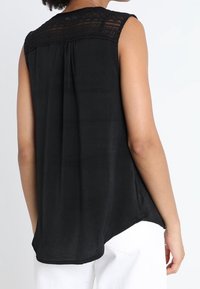 Mustat hihattomat paidat, jotka on valmistettu pehmeästä kankaasta ja joissa on pitsiyksityiskohta, pleated takaosa ja pyöristetty helma sivuaukkoineen.