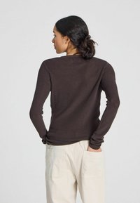 Maglione marrone a costine con maniche lunghe e scollo rotondo, caratterizzato da una silhouette aderente e una morbida consistenza. Indossato con pantaloni di colore chiaro.