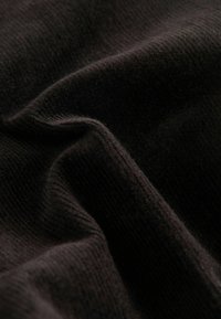 Zwart gebreide stof met een zachte, gestructureerde oppervlak die subtiele ribbels vertoont. Het materiaal lijkt warm en uitnodigend, met zichtbare vezels.