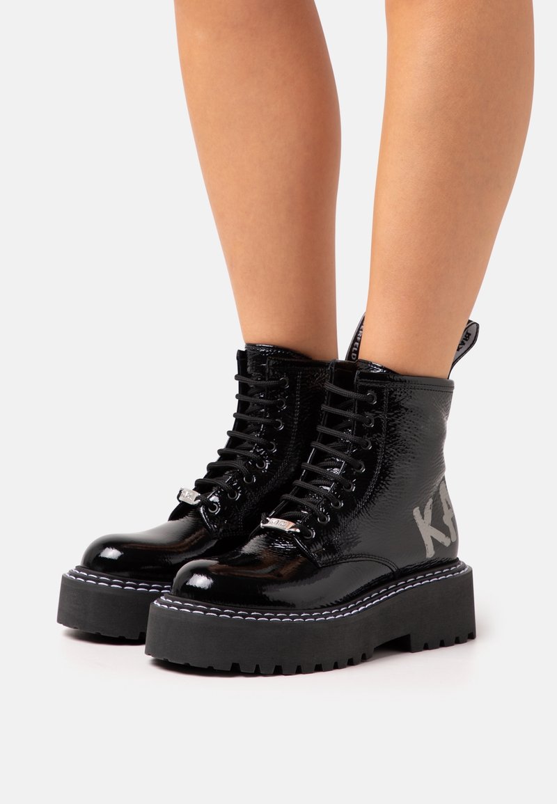 Black patent leather combat boots with a thick black platform sole, silver eyelet hardware, and "KAI" printed on the side.