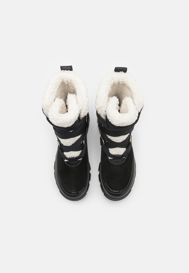 Czarne zimowe buty z grubym, białym sztucznym futrem, z czarnymi rzemykami, mosiężnymi zdobieniami i teksturowaną gumową podeszwą.