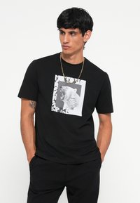 Black cotton t-shirt featuring a graphic of a roaring polar bear on a white background, framed with a geometric pattern. Short sleeves.