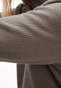 Pull tricoté marron clair avec une surface texturée, doté d'un col montant et d'épaules tombantes, présentant une coupe ample et décontractée.