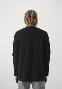 Suéter negro de punto con un patrón texturizado, mangas largas y cuello redondo. Puños y dobladillo terminados, adecuado para el uso casual.
