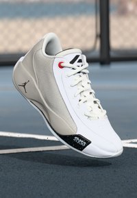 Baltas un pelēks sporta apavu modelis ar teksturētu virsu, melni un sarkani akcenti un logo sānos. Iekļauts mīksts apmale un šņorēšana.