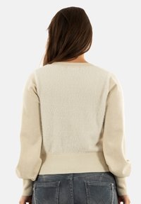 Maglione chiaro in crema con retro texturizzato, maniche lisce e orlo a coste. Materiale morbido con un design semplice e lineare.