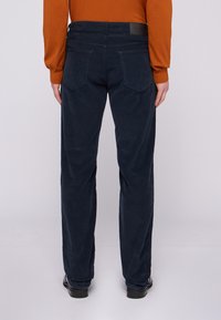 Pantalones de corduroy azul marino con corte recto, cinco bolsillos, textura sutil y un parche de marca negro en la cintura.