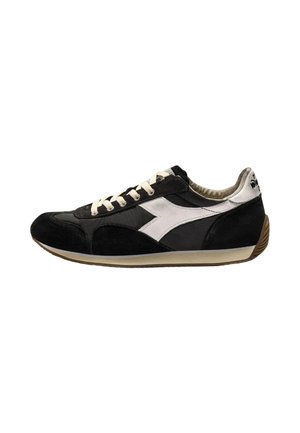 Zwart-witte lage sneaker met witte veters, een wit zijlogo en een beige zool met een bruine gestructureerde hiel.