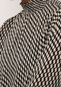 Zwart en crèmekleurig bedrukte stof met een hoge halsontwerp en een geruit motief, voorzien van een gestructureerde afwerking.