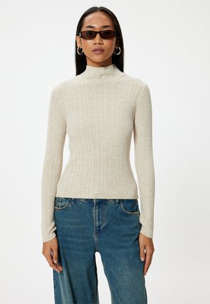 Geribde coltrui in lichtbeige, gemaakt van een gemêleerde stof. Lange mouwen, aansluitend ontwerp, gecombineerd met losse blauwe jeans.