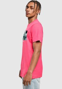 Rožinė medvilninė marškinė su apvaliu iškirpimu ir trumpomis rankovėmis, su grafiniu dizainu ant krūtinės. Kasdienis siluetas.