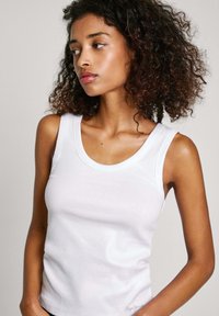 Top in cotone bianco senza maniche con texture a coste, scollo a barca e spalline larghe. Presenta un logo discreto all'orlo. Design semplice, forma aderente.