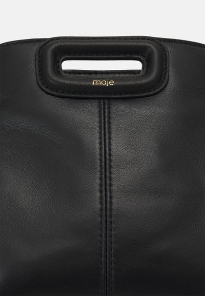 Schwarze Lederhandtasche mit einem auffälligen Ausschnittgriff und goldener Markierung. Glatte Textur mit vertikaler Nahtdetail. Elegantes und minimalistisches Design.