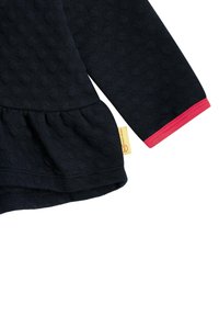 Maglietta a maniche lunghe di un blu scuro con un motivo a pois testurizzati, orlo a peplum e polsini in contrasto rosa. Presenta un piccolo etichetta sull'orlo.