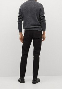 Jean foncé avec une coupe slim et poches arrière, associé à un pull en tricot gris, vu de dos, avec des poignets et un ourlet côtelés.