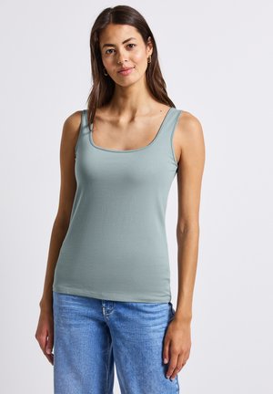 Helles grünes Tanktop aus weichem Stoff, mit einem quadratischen Ausschnitt und breiten Trägern. Kombiniert mit hellblauen Jeans.