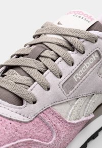 Sapatilhas Reebok clássicas nas tonalidades de rosa e cinza. Apresentam material de camurça texturizado, atacadores planos e um patch com o logótipo na língua.