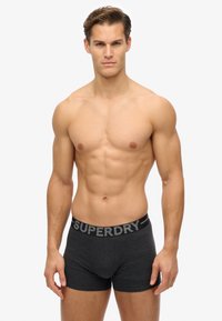 Grijze katoenen boxershorts met een brede zwarte tailleband met het merk "SUPERDRY" in contrasterende zilveren lettering. Soepele textuur, aansluitend ontwerp.