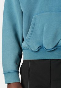 Blauer, strukturiertes Sweatshirt mit einer Tasche vorne, gerippten Bündchen und einem gewellten Saum. Hat einen kontrastierenden schwarzen Akzent am unteren Ende.