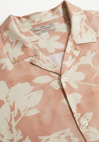 Chemise rose clair à col avec motif floral blanc, ouverture à boutons sur le devant, et étiquettes "MNG MAN" et "Regular Fit" à l'intérieur du col.