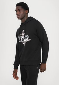 Sweatshirt preto feito de tecido macio com capuz ajustável. Apresenta uma impressão gráfica branca na frente. Punhos e bainha canelados.