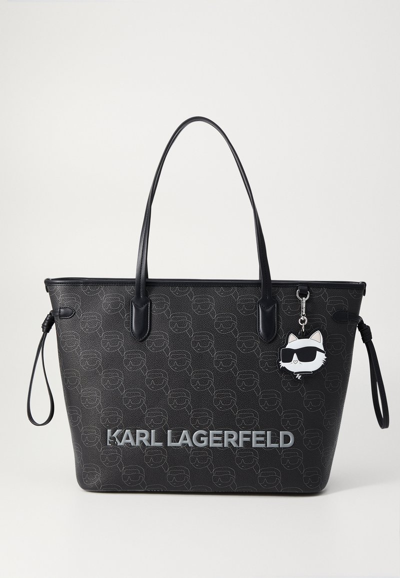 Black tote bag featuring an embossed pattern of faces, leather handles, silver "KARL LAGERFELD" branding, and a cartoon cat charm.
