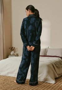 Navy blue floral-patterned pajamas with white piping, featuring a button-up shirt and loose-fitting pants. Soft fabric texture.