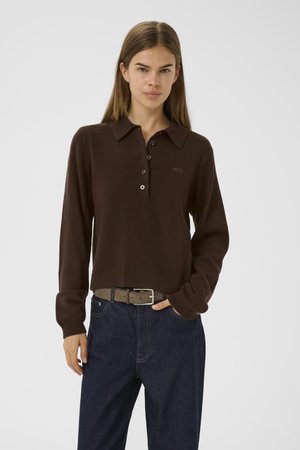 Brown long-sleeve polo shirt with a collar, five buttons, and subtle logo detail; paired with dark blue denim jeans and a textured belt.