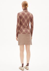 Langarm, aansluitend shirt in een bruine geruite patroon, met een hoge kraag. Gepaard met een beige corduroy rok en crèmekleurige sokken met rode accenten.