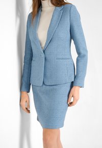 Hellblauer, strukturierter Blazer kombiniert mit einem eng anliegenden Bleistiftrock. Der Blazer verfügt über einen einzelnen Knopfverschluss und aufgeschlagene Revers.