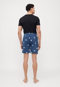 T-shirt noir à manches courtes avec col rond, assorti à un short de bain bleu arborant un motif de texte audacieux répété en bleu clair et noir.