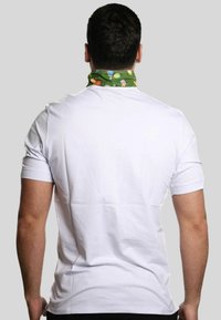 T-shirt bianco a maniche corte visto da dietro, con una sciarpa verde al collo decorata con motivi colorati a tema tennis. Tessuto di cotone liscio.
