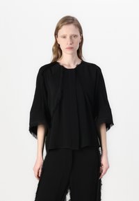 Black top with wide sleeves, featuring fringed edges, a round neckline, and a loose fit. Paired with matching black pants with fringe accents.