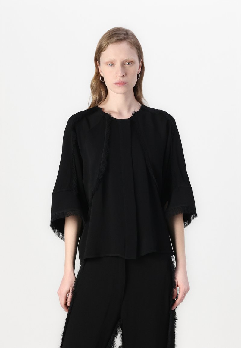 Black top with wide sleeves, featuring fringed edges, a round neckline, and a loose fit. Paired with matching black pants with fringe accents.