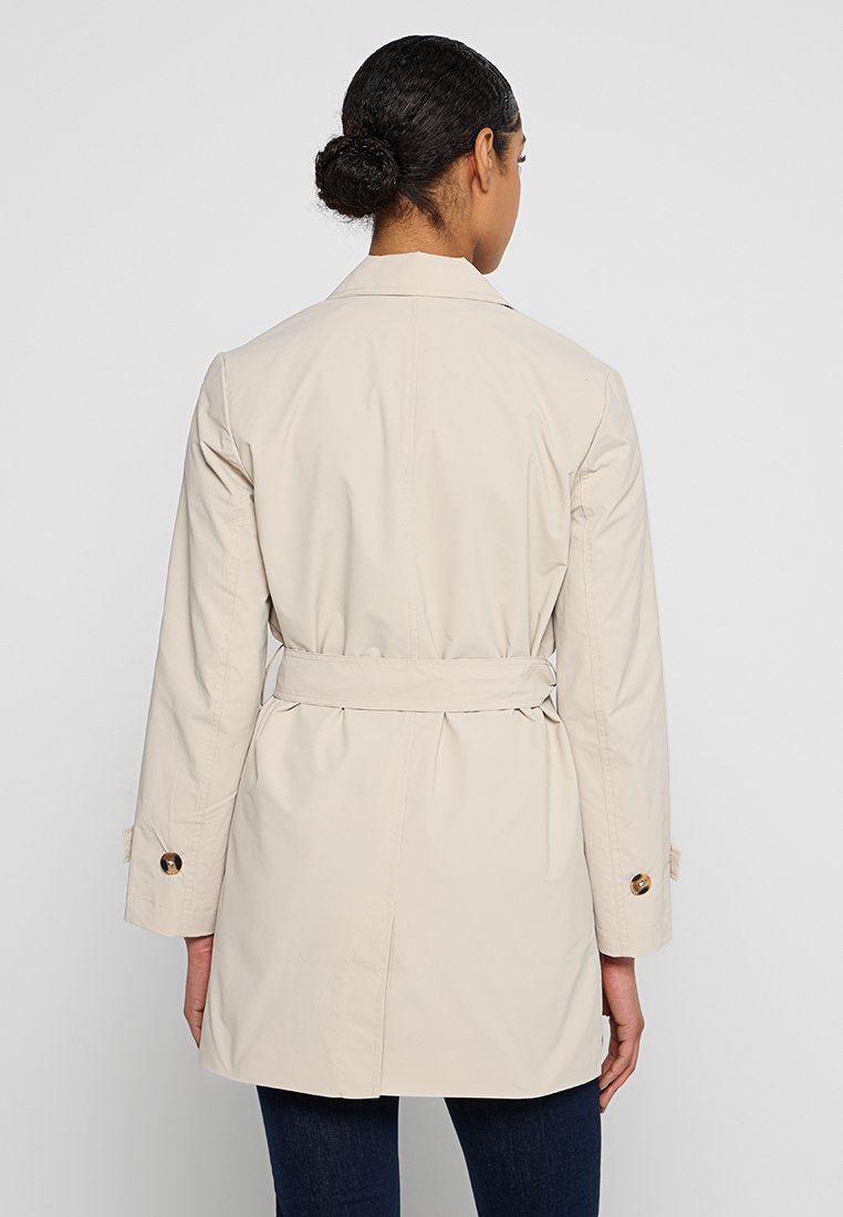 Abrigo trench beige con cintura ceñida, diseño de doble botonadura, detalles de botones y mangas largas, visto desde la parte de atrás. Textura suave.