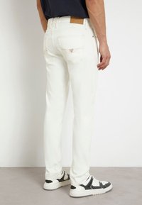 Jeans blancos con un corte ajustado, diseño de cinco bolsillos y detalles de costuras claras. La tela tiene una textura suave, complementada con una cinturilla de cuero marrón.