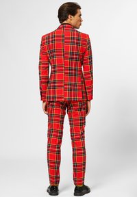 Red plaid suit consisting of a fitted jacket and matching trousers. Features black and yellow lines in a checkered pattern. Details include a smooth texture and structured design.
