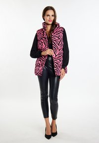 Różowa i czarna kamizelka puffer w zebra z wysokim kołnierzem, zapinana na zamek z bocznymi kieszeniami, w połączeniu z błyszczącymi czarnymi skórzanymi spodniami i szpilkami.