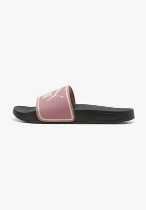 Schwarze Slidesandale mit einem strukturierten pinken Riemen, auf dem ein beiges Puma-Logo und der eingeprägte Puma-Schriftzug an der Sohlen-Seite zu sehen sind.