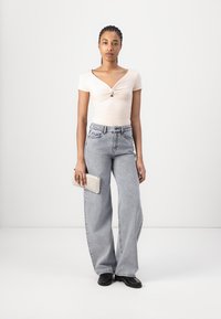 Top rosa chiaro a maniche corte con fronte attorcigliato, abbinato a jeans grigi chiari a gamba larga. Una borsa a tracolla texture e scarpe nere completano il look.