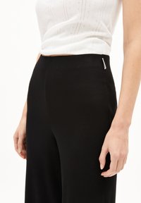 Zwarte geribbelde gebreide broek met een hoge tailleband, voorzien van een zijlabel en een aansluitende pasvorm, gecombineerd met een witte textuur crop top.