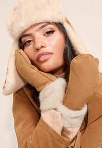 Pruuni kunstkarvaga müts ja sõrmikud beežide aktsentidega, pehme tekstuuri, sooja kangaga ja lõdva lõikega, sobitatud heledabeebi topiga.