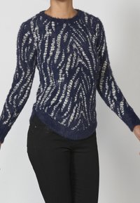 Suéter esponjoso azul marino con patrón de zigzag blanco, cuello redondo y mangas largas, con un corte relajado y dobladillo curvado.