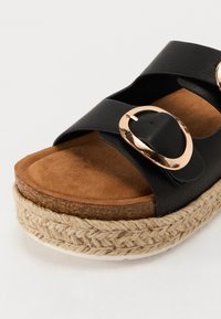 Schwarzer Kunstleder-Sandalette mit zwei breiten Riemen und einer metallisch goldenen Schnalle. Hat ein Fußbett aus braunem Wildleder und eine geflochtene Jute-Plattformsohle.