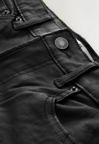 Sorte denimjeans har fremtrædende syninger, en metal knaplukning og en glat tekstur med en sidelomme.