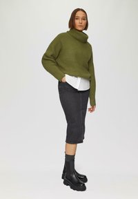 Groene chunky gebreide coltrui, witte button-up shirt eronder, zwarte denim kokerrok en zwarte platform enkellaarsjes.